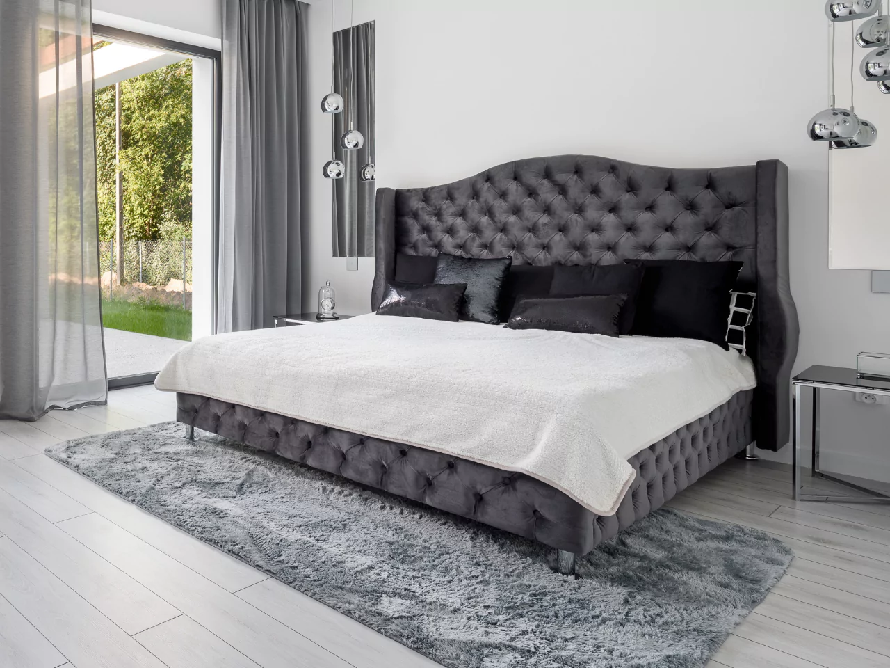 Tempat tidur king size dengan headboard mewah dan seprai elegan di kamar tidur luas.